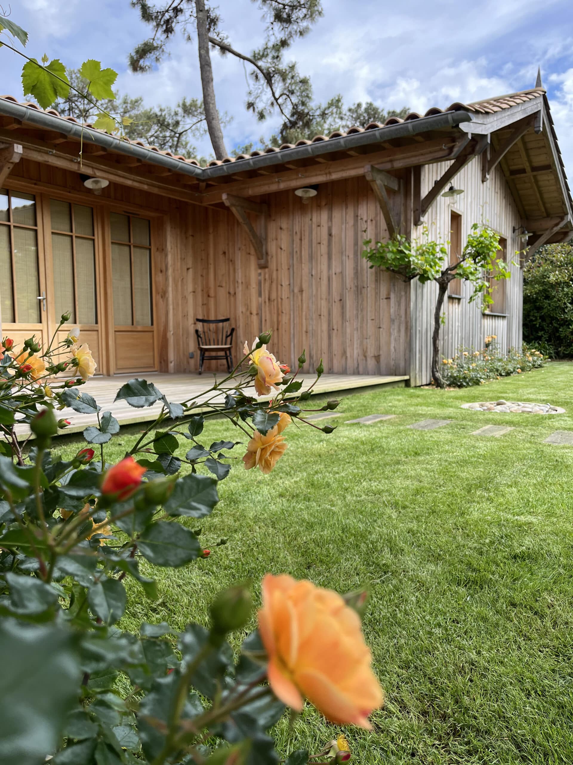 Vue basse d'un jardin avec roses oranges vives et pelouse bien entretenue menant à une cabane en bois clair avec terrasse.